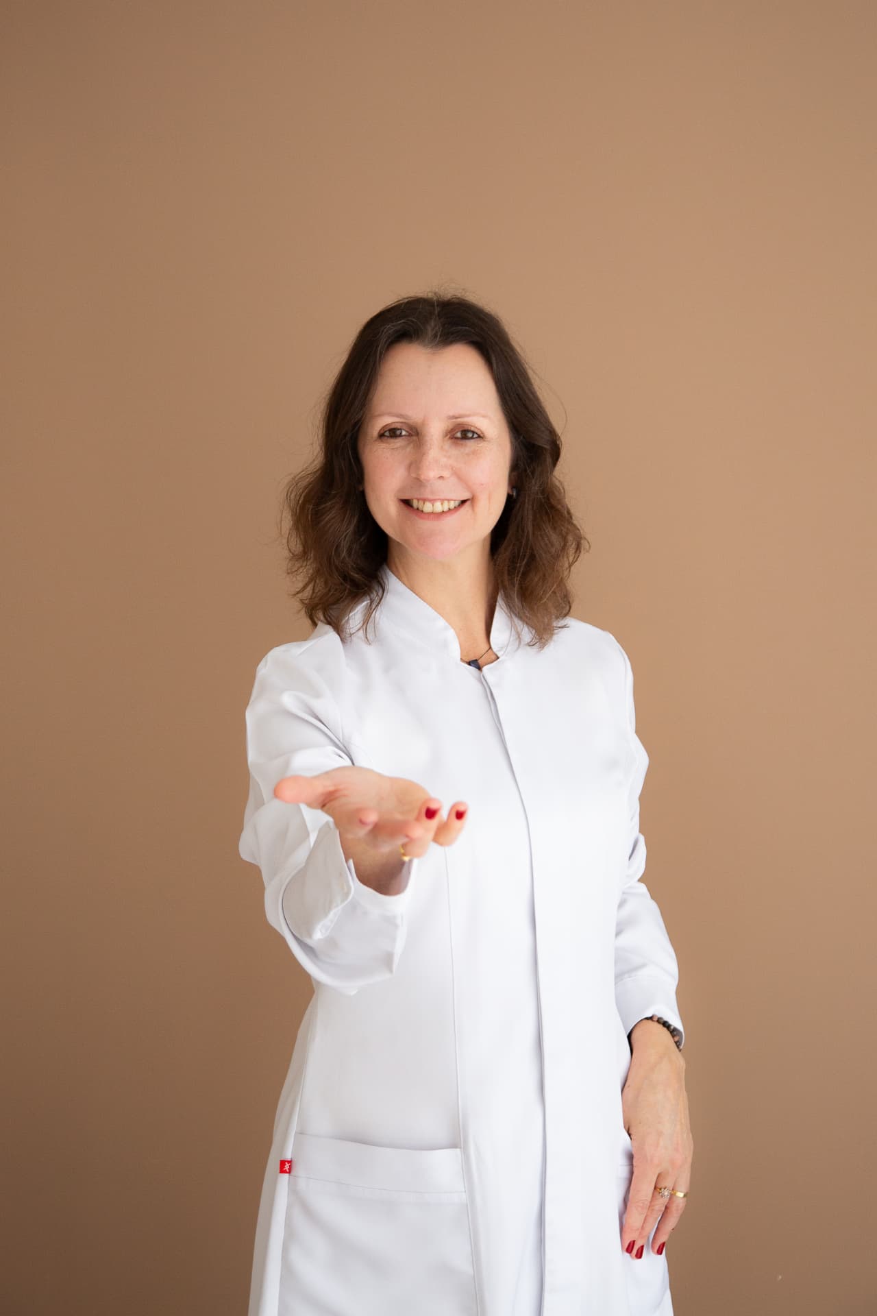 Luciane de jaleco branco estendendo a mão em gesto acolhedor